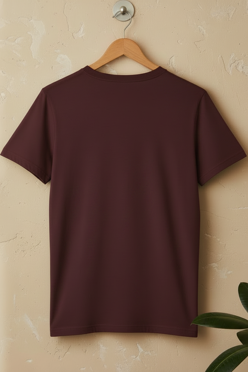A maroon short-sleeve t-shirt hanging on a wooden hanger against a textured beige wall. The shirt features a cream-colored graphic of a winged angel standing on clouds with the text 'DIVINE GRACE' printed below.