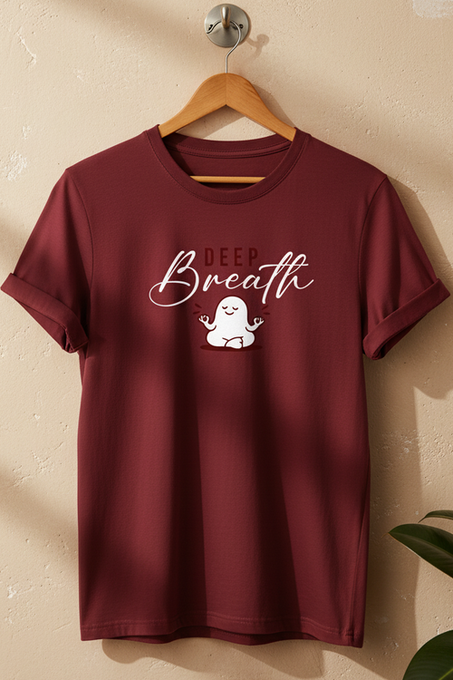 A maroon short-sleeve t-shirt hanging on a wooden hanger against a textured beige wall. The shirt features a white graphic print on the chest that reads 'DEEP Breath' above a small cartoon ghost meditating.