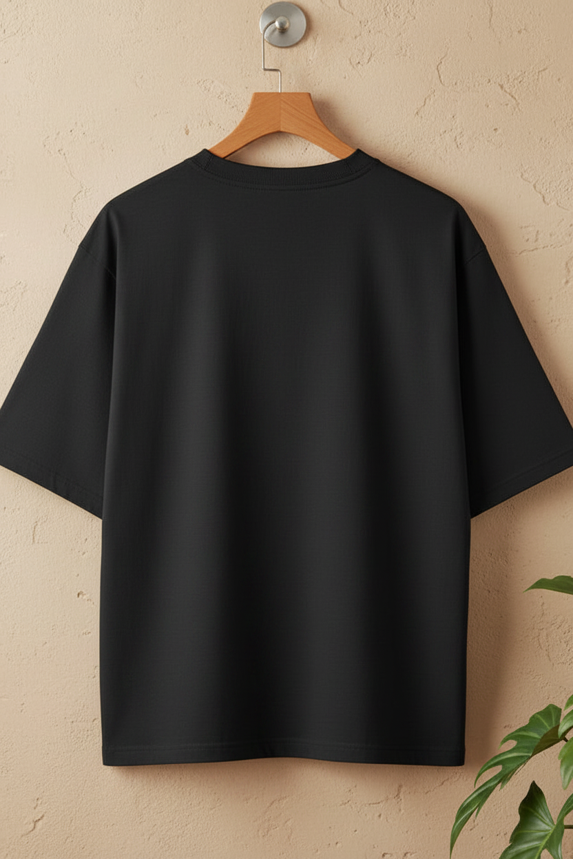 A plain black short-sleeve T-shirt hanging on a wooden hanger against a textured beige wall, with a small green plant visible in the lower right corner.
