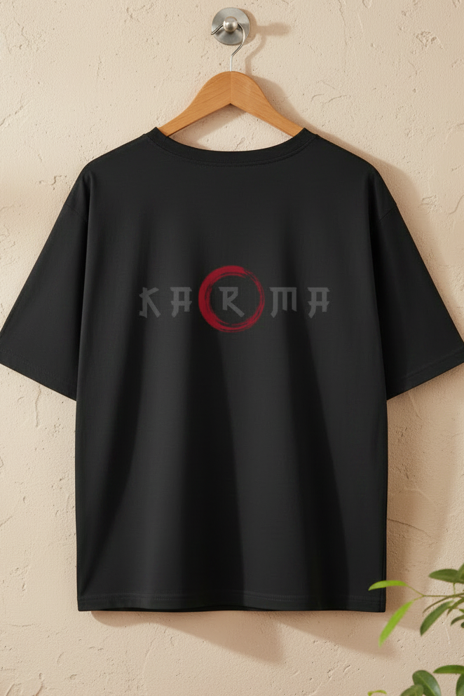 A black short-sleeve t-shirt hanging on a wooden hanger against a textured beige wall. The shirt features a stylized graphic on the chest with the word 'KARMA' in gray letters, where the letter 'A' is enclosed in a red circle.